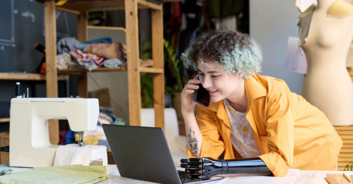 A woman with prosthetic arm talking on phone and using laptop